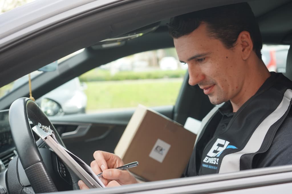 Delivery driver writing on clipboard inside a courier vehicle